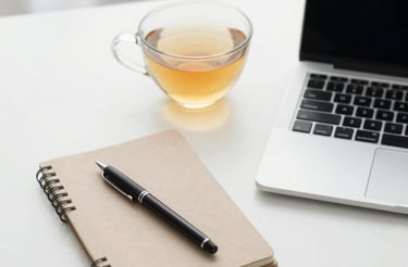 A calm workspace with a laptop, a cup of tea, and a soft beige notebook beside a small potted plant.