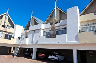 Modern multi-story apartment complex with covered parking and silver chimney flues under a clear blue sky.