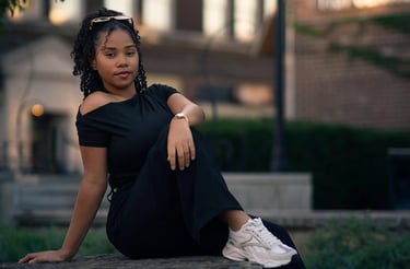 Retrato urbano de una joven mujer sentada sobre una roca al atardecer, con fondo de edificios y luz 