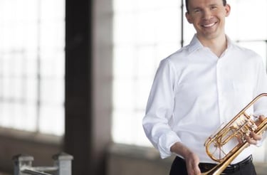 Man wearing white button down shirt, holding a trumpet and smiling.