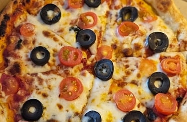 Freshly baked pizza with melted mozzarella cheese, black olives, and cherry tomatoes in a cardboard box.