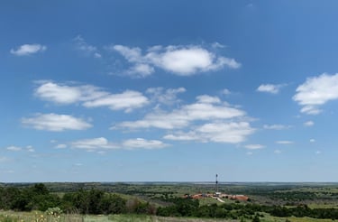A distance view of a drilling rig on a grassy field in Oklahoma under a blue sky with clouds.