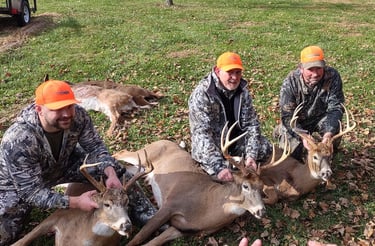 Three hunters posing in a field with multiple harvested whitetail bucks.
