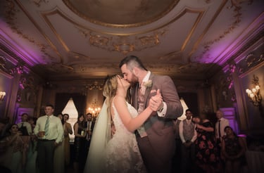 Newlywed bride and groom sharing a romantic first dance and kiss in an elegant, ornate ballroom.