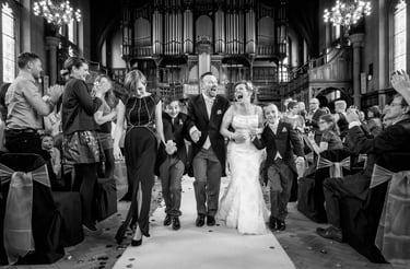 Black and white photo of a happy bride and groom walking down the aisle after a church wedding ceremony.