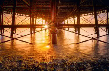 the sunrising through the structure under the pier. sun reflecting on the sea