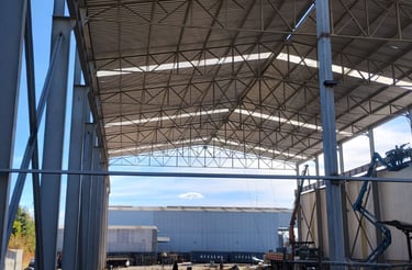 Estrutura metálica de galpão industrial em montagem, com cobertura treliçada e pilares aparentes.