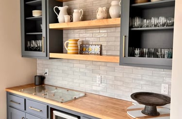Modern home bar featuring gray cabinets, wooden countertops, and open shelving with subway tile backsplash.