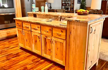 Rustic kitchen island with knotty pine cabinets and granite countertops over rich hardwood floors.