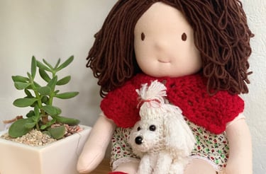 Muñeca de tela hecha a mano con cabello de estambre castaño, sosteniendo un perrito blanco tejido
