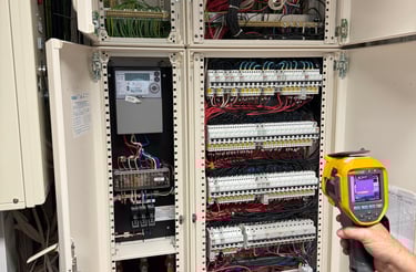 Technician using a thermal imaging camera for electrical inspection of an open circuit breaker panel.