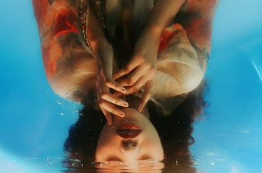 Retrato artístico invertido de uma mulher submersa em água azul clara com reflexos e bolhas.