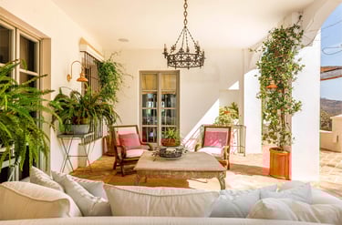 Terrace with wooden seating, pink cushions, plants, and a chandelier in rustic style.