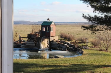 Paysage de campagne avec un lac paisible, une petite cabane en bois au bord de l'eau, et une chute d