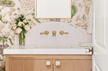 Elegant bathroom vanity with floral wallpaper, gold mirror, and marble countertop.