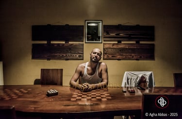 Person in white tank top with clasped hands at checkerboard table in dimly lit room.