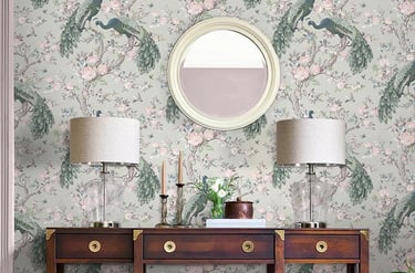 Elegant peacock floral wallpaper behind a dark wood console table with table lamps and a round mirror.