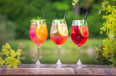 Drei bunte Aperitifs im Freien, Orange, Gelb, Rot. Frische Minze, Limetten & Strohhalme. metta-macro
