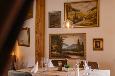Rustikaler Fine-Dining-Tisch mit Landschaftsgemälden und warmer Kugel-Pendelleuchte.