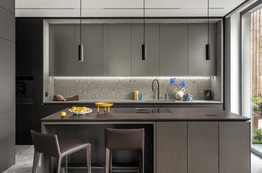 Minimalistyczna wyspa kuchenna, czarna armatura, blat i ściana wykończone szarym lastryko.