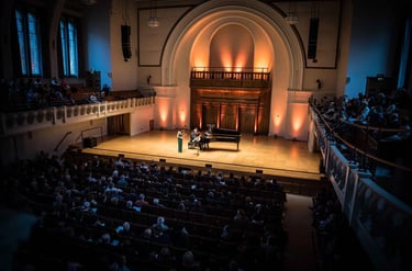 Musicians performing a classical concert on stage with a grand piano in a crowded theater venue.