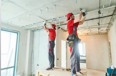Two construction workers installing a metal ceiling frame in a room under renovation.