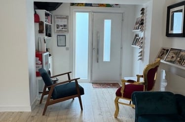 Modern studio entryway featuring light oak flooring, velvet armchairs, and framed family portraits.