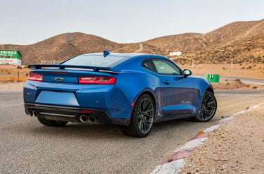 Chevrolet Camaro ZL1 azul visto por trás em pista cercada por montanhas desérticas