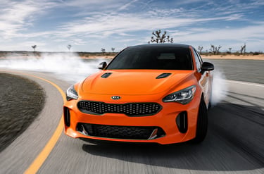 Kia Stinger laranja fazendo drift em pista com fumaça nos pneus.
