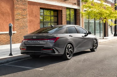 Hyundai Elantra 2026 cinza estacionado em rua urbana iluminada diante de edifícios.