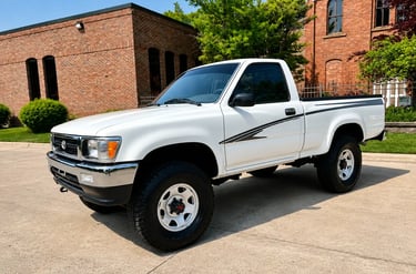 Toyota Hilux cabine simples branca dos anos 90 estacionada em área urbana arborizada