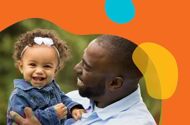 Man cheerfully holding his daughter in a frame of orange yellow and blue organic shapes.