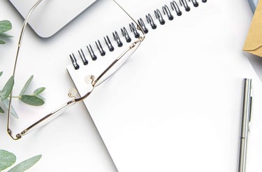 Image of a pair of glasses on top of a notepad, with a pen and a eucalyptus branch