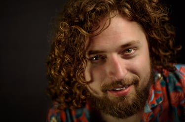Close-up portrait of a smiling man with long curly brown hair and a beard.