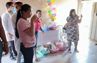 A woman speaking at a community event with health kits and colorful balloon decorations.