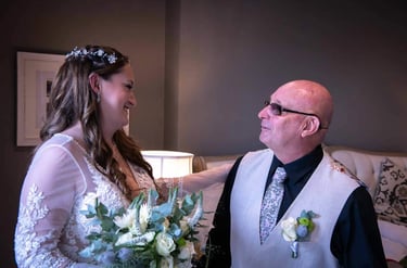 Smiling bride in lace wedding dress holding a bouquet while looking at her father during a first look.