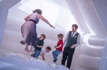Wedding guests and children jumping inside a white inflatable bouncy castle at a wedding reception.