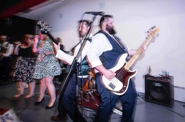 Live wedding band performing on stage with a bassist, guitarist, and singers at a reception venue.