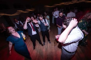 Wedding guests dancing and drinking on a dimly lit dance floor during a lively wedding reception.