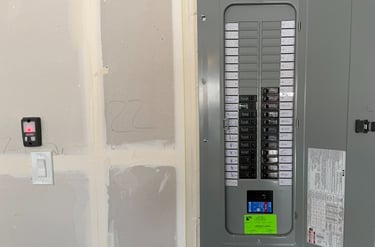 A residential electrical panel box with circuit breakers installed on a drywall surface.