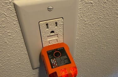 An orange GFCI outlet tester plugged into a white wall socket to check for proper electrical wiring.
