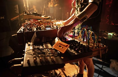 Electronic music artist performing live with a modular synthesizer, patch cables, and analog gear.