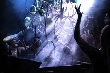 Performers interact with a surreal, smoky wire sculpture during a dark experimental theater production.