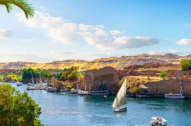 Traditional felucca sailboat and cruise boats on the Nile River in Aswan, Egypt near historic ruins.