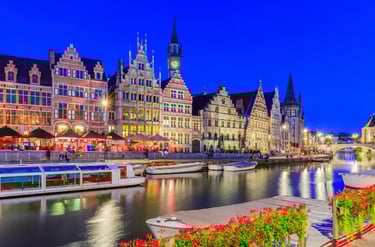 Illuminated medieval guildhouses and canal boats at Graslei and Korenlei in Ghent, Belgium at twilight.