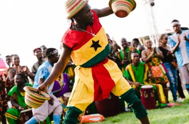 A Ghanaian performer in a traditional flag costume dances with woven hats during a cultural festival.