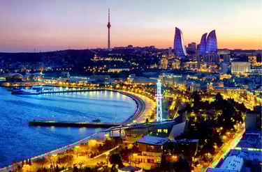 Illuminated Baku city skyline at sunset featuring the Flame Towers and Caspian Sea coastline.