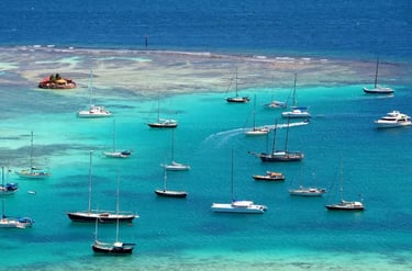Aerial view of sailboats and catamarans anchored in the turquoise Caribbean waters of a tropical island bay.