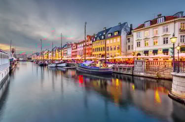 Colorful historic buildings and wooden boats in Nyhavn canal, Copenhagen, at twilight.