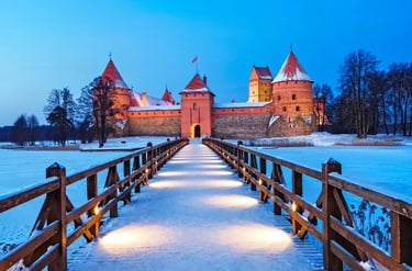 Illuminated Trakai Island Castle in Lithuania at twilight during winter with a snow-covered bridge and frozen lake.
